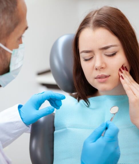 Woman visiting dentist for emergency dentistry holding cheek in pain
